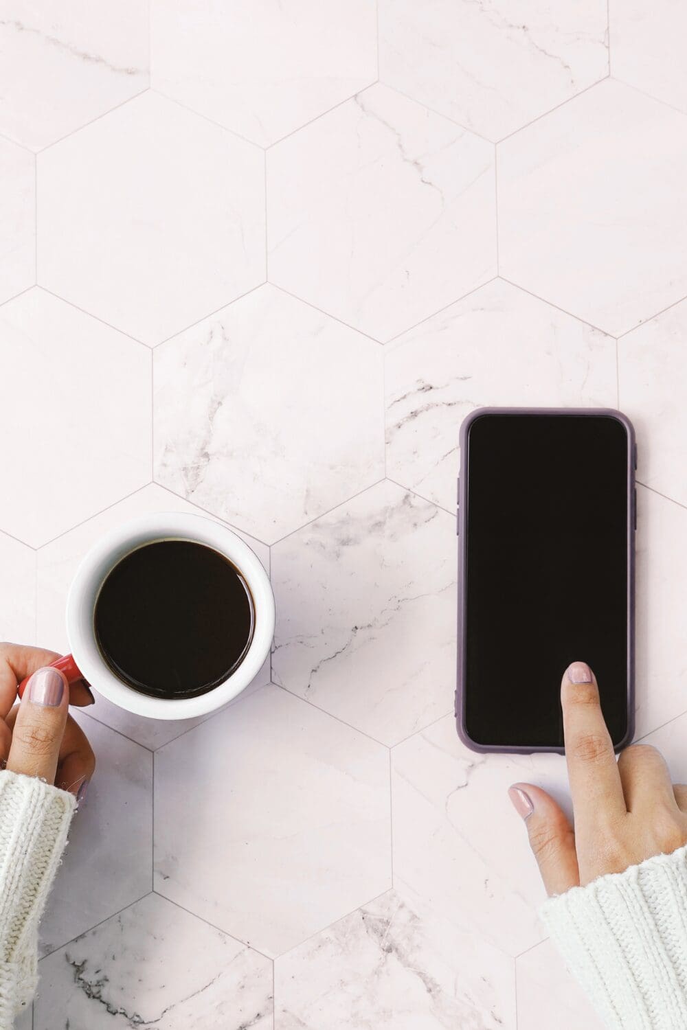 Image of a females hands holding a black coffee and iphone - the blog is about email phrases and how to best word them